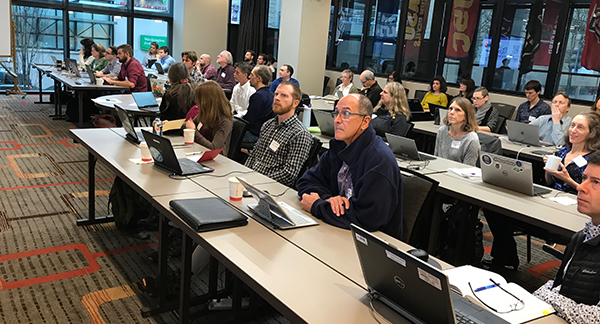 People sit at rows of tables with open laptops during the workshop