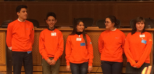 5 teens in orange sweatshirts stand on stage at PERSEUS meeting