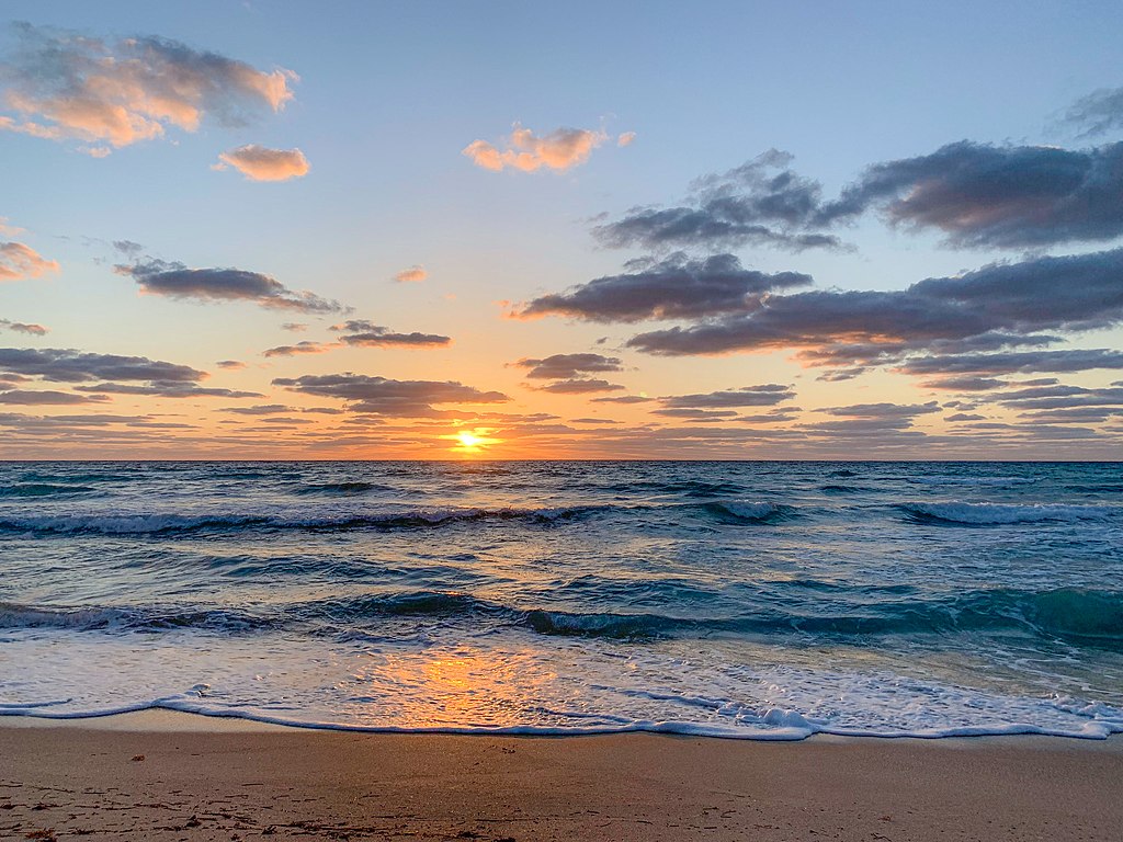 The sun hangs low over the ocean horizon, with a strip of sandy beach in the foreground.