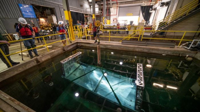 People in hard hats stand by a yellow guardrail looking down into a test pool below.