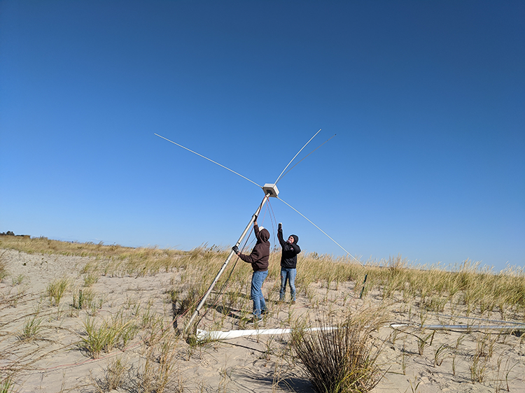 two people standing up a high-frequency radar antenna on a beach.