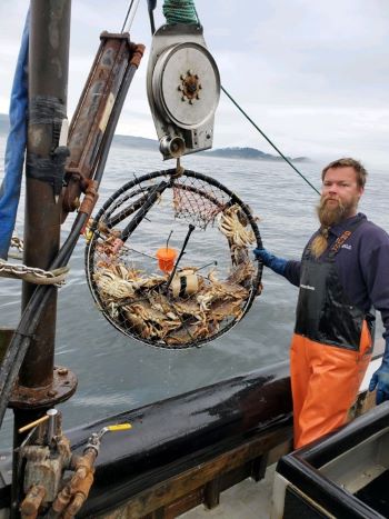 Fisherman shows a crab pot hanging above deck containing a sensor.